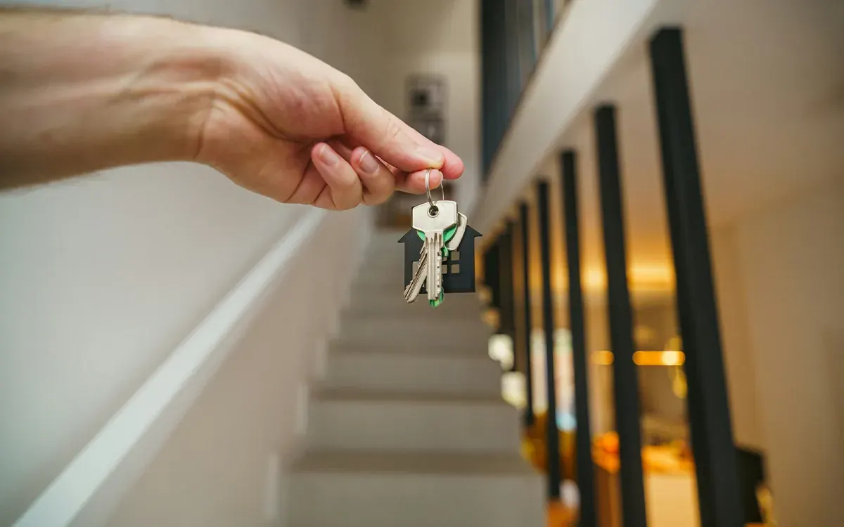 Mano entregando las llaves de una vivienda recién terminada junto a una escalera