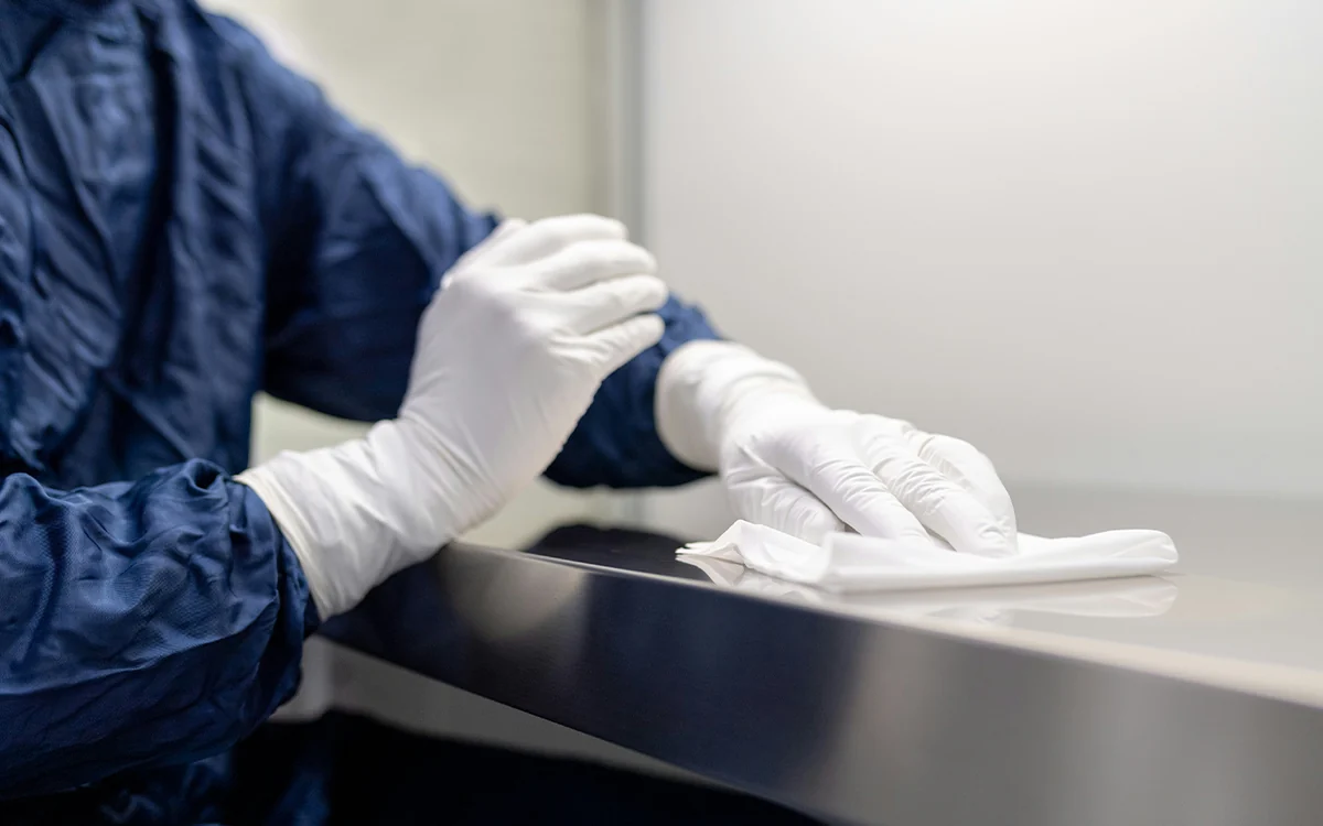 Técnico con guantes desinfectando una superficie de acero inoxidable durante la sanitización de un espacio
